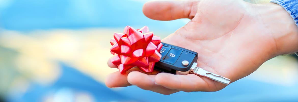 Hand holding a car key with a small red bow on it