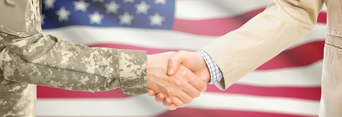 Members of the military shaking hands in front of American flag.