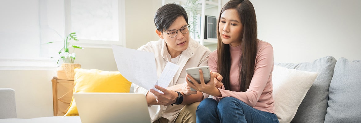 Two people sitting with a calculator and laptop reviewing paper work.