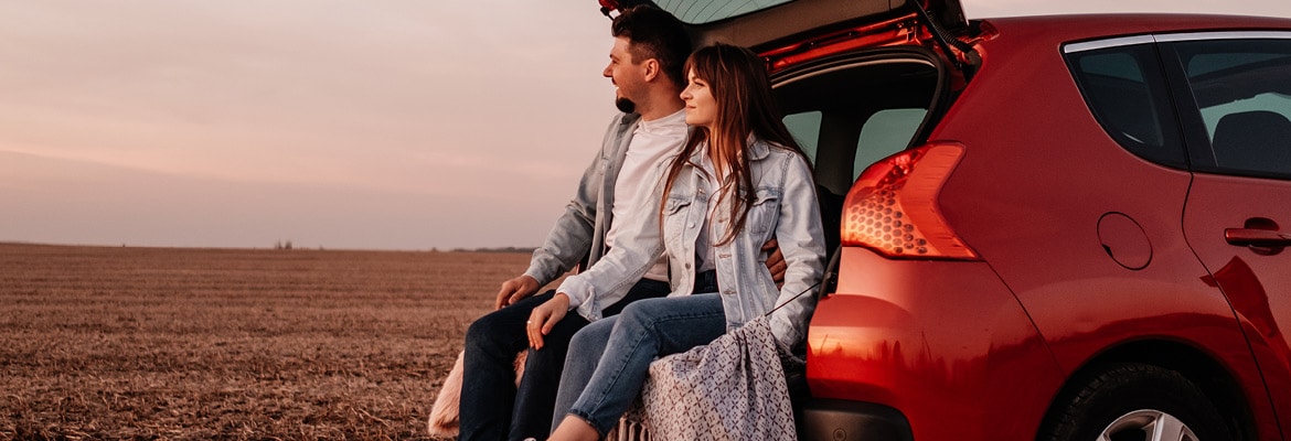 A man in a woman sitting in a car looking at a scenic landscape.