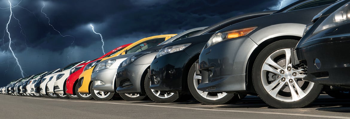 Line of new cars at a dealership during a lightning storm.