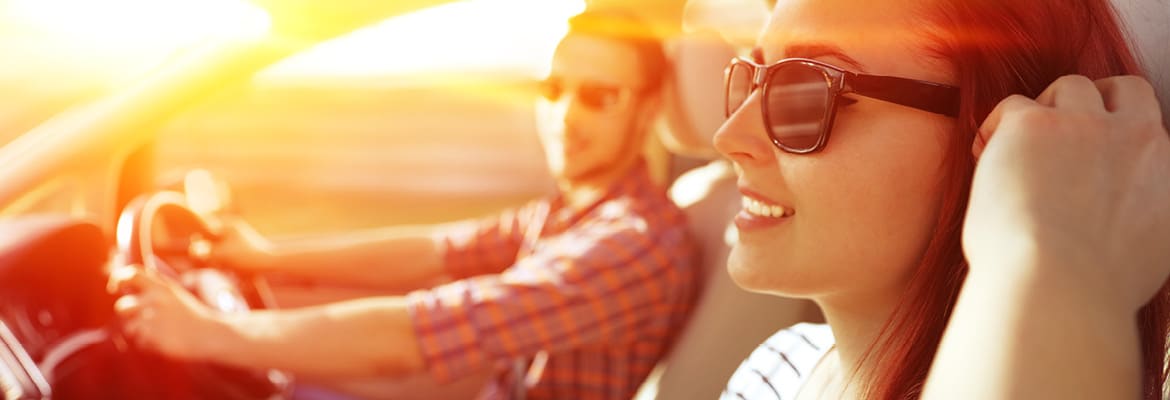 Picture of a man and a woman driving a car and wearing sunglasses.