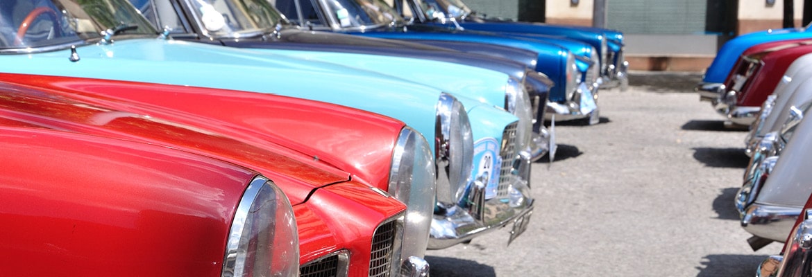 Several classic and collector cars parked outside in a parking lot.