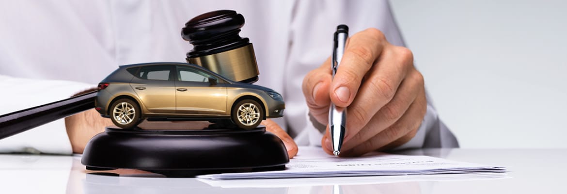 Gavel and silver SUV sitting on sound block while person signs contract.