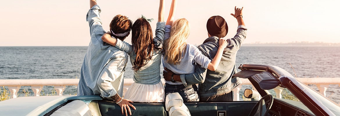 Gen Zers leaning on the side of a convertible overlooking the ocean.