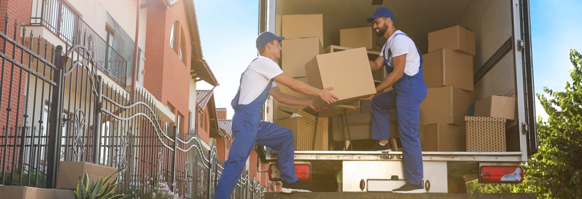 Two professional movers loading cardboard boxes into the back of a moving truck.