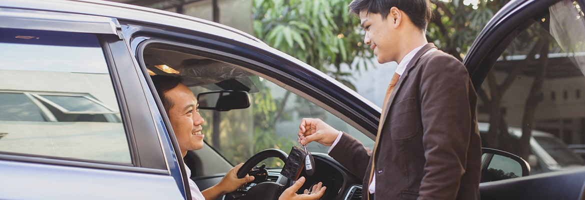 A man in the driver's seat of a car receiving keys from a salesperson.