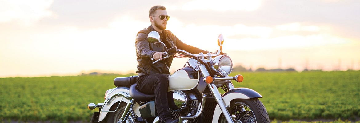 Man on a motorcycle driving past a green field.