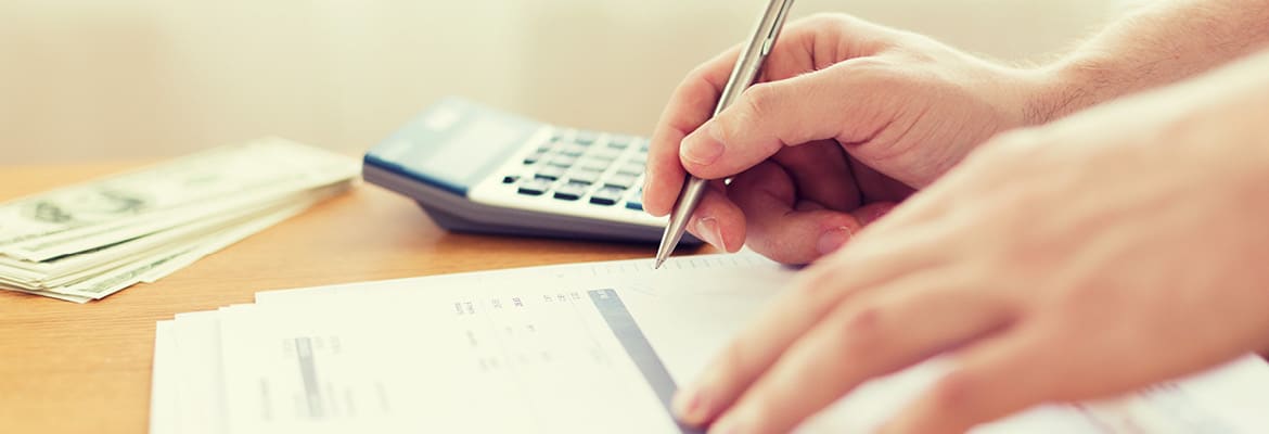 Close up of a person's hands with pen and calculator, working on tax papers