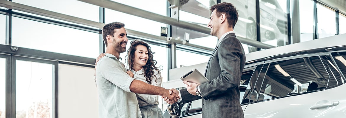 Couple shaking hands with car salesman