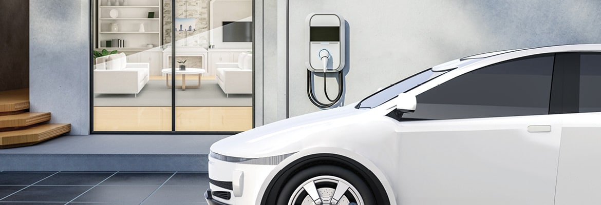 A white electric vehicle parked outside of a home, plugged into an EV charger