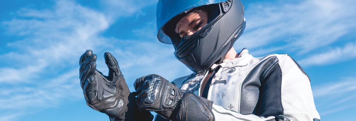 A motorcycle rider wearing a helmet, pulling a glove on to their hand