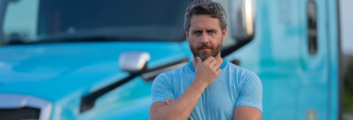Male truck driver standing confidently in front of his bright blue truck.