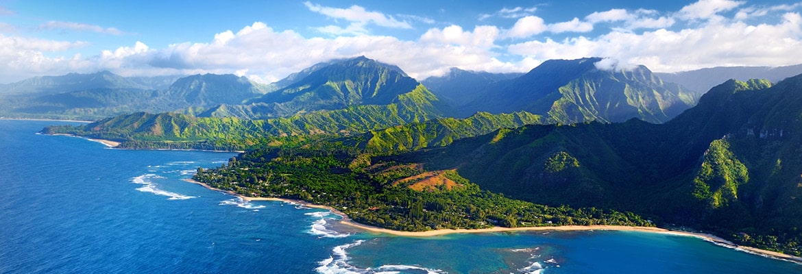 A color photo of a Hawaiian island with blue water and green mountains.