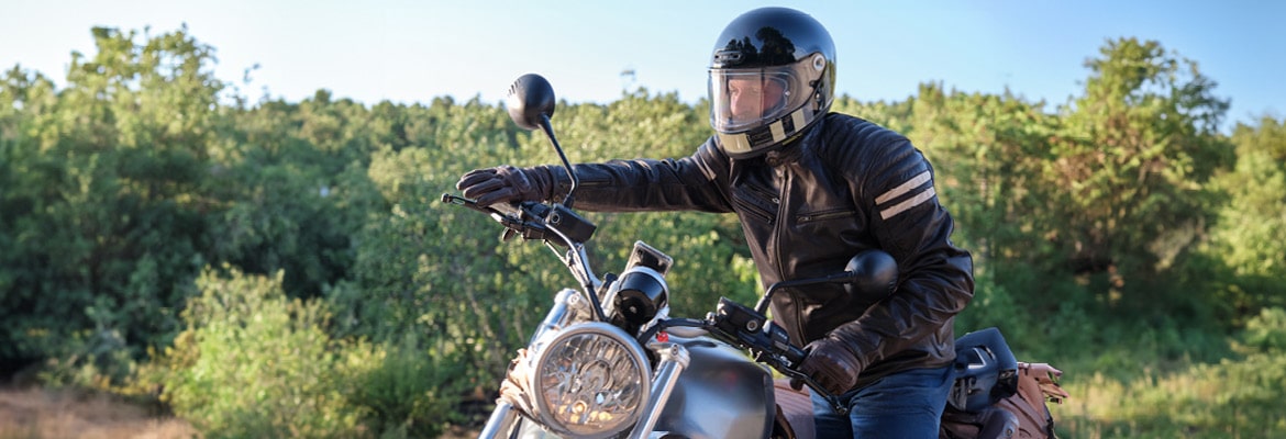 Man riding a motorcycle wearing a helmet and dressed in riding gear.