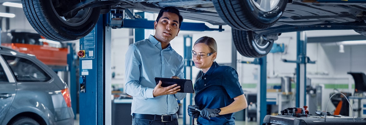 An auto technician and mechanic looking at a car and tablet.