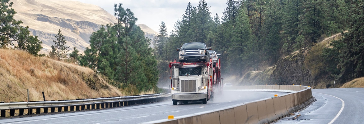 Picture of an open transport car carrier driving on a rural highway