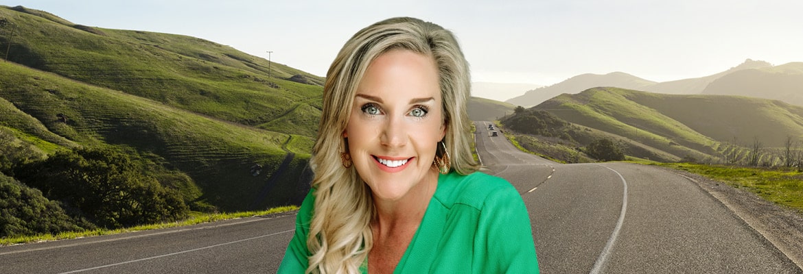 Image of Mary Bartlett of Montway in front of a road running through green mountains.