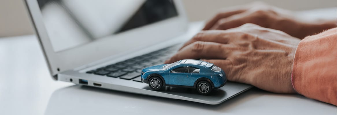 Hands on a laptop next to a toy car, possibly buying a vehicle on CarStory