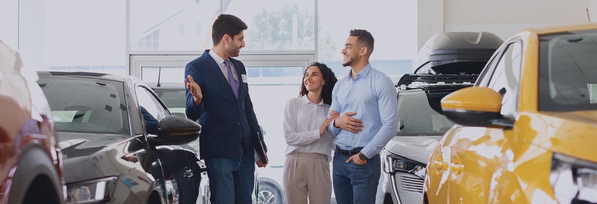 A young couple speaking with a salesperson inside a car dealership