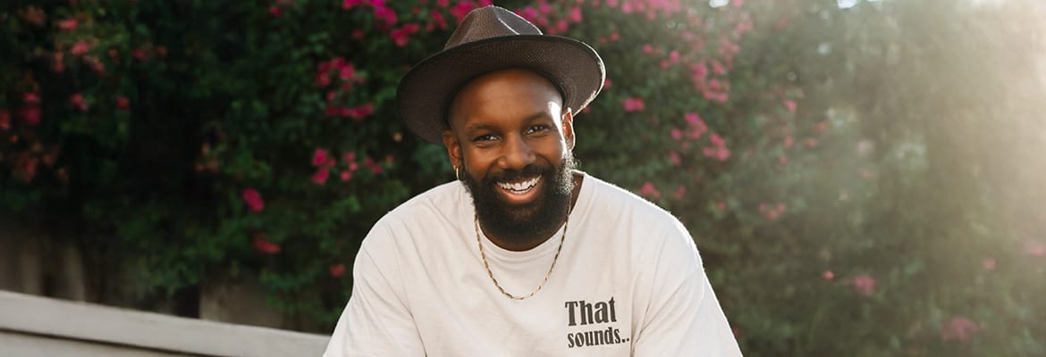 Elijah Holt sitting in an outdoor setting, smiling and looking at the camera.