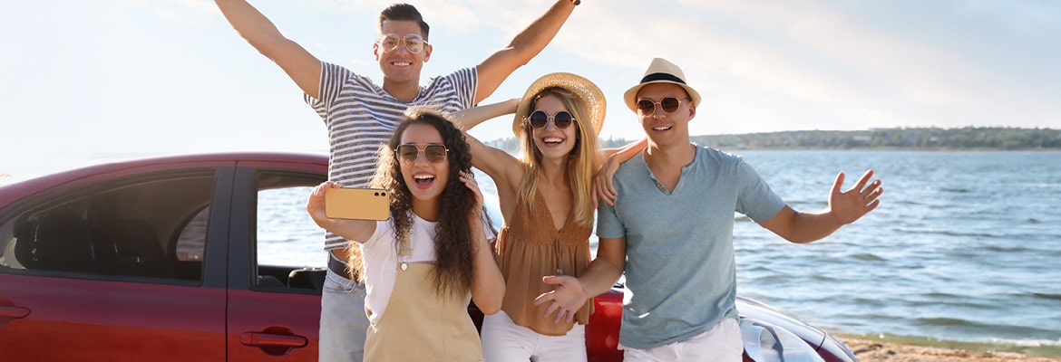 Small group of people taking a photo in front of their car at the beach