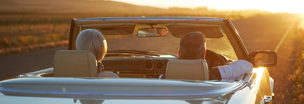 Snowbird couple driving convertible at sunset after shipping car.