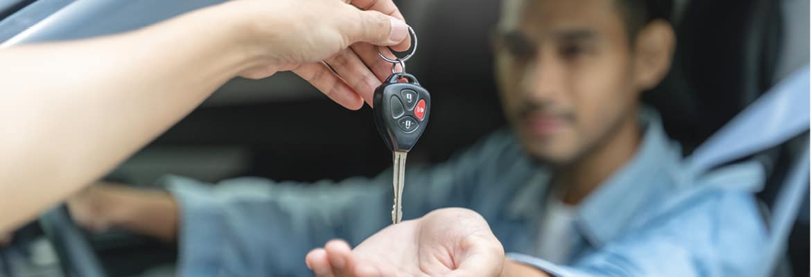 Car salesperson handing keys to man in certified pre-owned car.