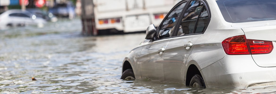 A white car submerged in flooded street after storm.