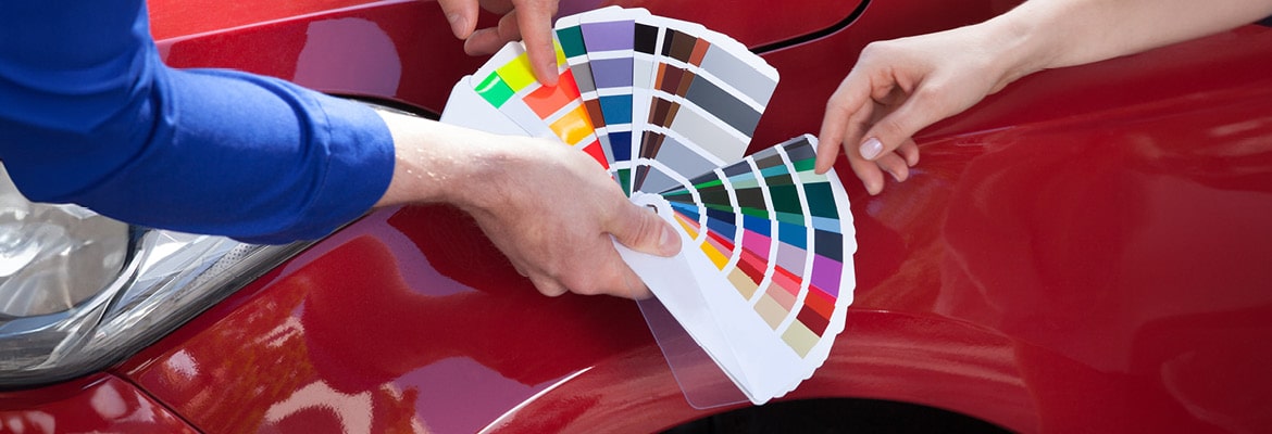 Car buyer holding up popular color options against red car.