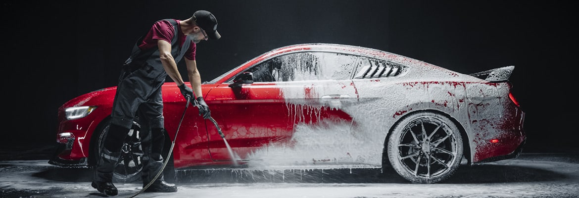 A man professionally detailing a car, cleaning soap off with a hose.